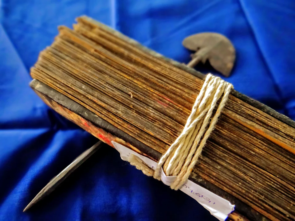 A bundle of Odia palm-leaf manuscript pages tied with string, beside an iron lekhani stylus